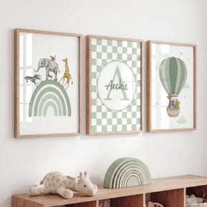 May include: Three framed wall art prints featuring sage green accents. The first shows a zebra, elephant, and giraffe on a rainbow. The second displays a checkered pattern with a large letter A and the name Archie. The third depicts a hot air balloon.