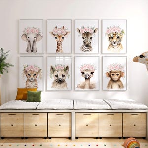 May include: A set of eight framed prints featuring watercolour illustrations of various animals wearing flower crowns. The animals include an elephant, giraffe, zebra, tiger, cheetah, ostrich, monkey, and hyena. The prints are displayed on a white wall above a wooden storage bench.