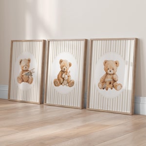May include: Three framed prints featuring watercolor illustrations of teddy bears. Each bear is depicted in a different pose, holding a toy airplane, a stuffed bunny, and a wooden train. The background has a striped pattern.
