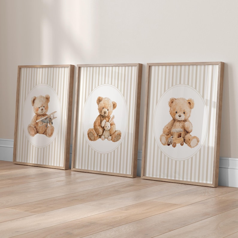 May include: Three framed prints featuring watercolor illustrations of teddy bears. Each bear is depicted in a different pose, holding a toy airplane, a stuffed bunny, and a wooden train. The background has a striped pattern.