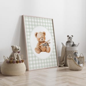 May include: A framed print featuring a watercolor illustration of a teddy bear holding a toy airplane. The background is a light green and white gingham pattern. Wicker baskets with stuffed animals are in the foreground.