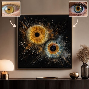 May include: A square wall art piece featuring two large, detailed human irises against a black background. The top left iris is golden-brown, while the bottom right iris is blue with a golden-brown centre. Splatters of gold and white paint surround both.