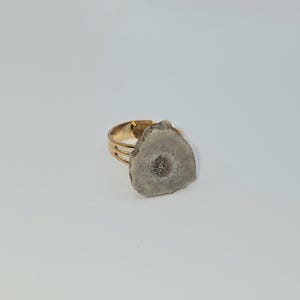 May include: A gold adjustable ring with a large, irregular shaped, light gray stone with a darker gray center.
