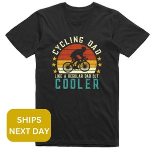 Pu&ograve; includere: Maglietta nera con una grafica in stile retr&ograve; che dice "Cycling Dad Like a Regular Dad But Cooler". La grafica presenta una silhouette di una persona che va in bicicletta con uno sfondo di tramonto.