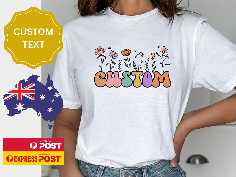 Op de afbeelding: Wit T-shirt met een kleurrijke afbeelding van het woord "CUSTOM" in een retro-lettertype met bloemen die uit de letters groeien.