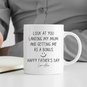 May include: White ceramic mug with a black printed message: "LOOK AT YOU LANDING MY MUM AND GETTING ME AS A BONUS" with a smiley face and "HAPPY FATHER'S DAY Love, Alice". The mug has a curved handle.