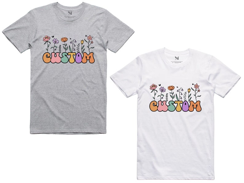 Op de afbeelding: Twee T-shirts met een bloemenontwerp en het woord "CUSTOM" in kleurrijke bubbelletters. De shirts zijn grijs en wit.