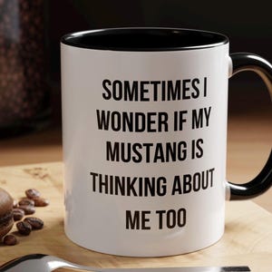 May include: White ceramic coffee mug with a black rim and handle. The mug has black text that reads "Sometimes I wonder if my Mustang is thinking about me too."