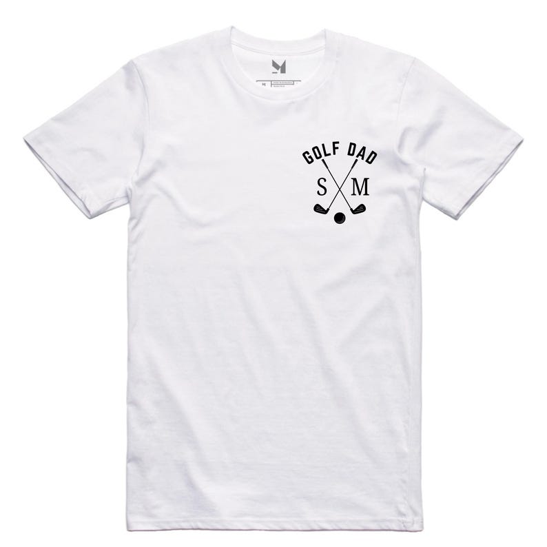 May include: White t-shirt with a black graphic of crossed golf clubs and the text "Golf Dad" with the letters "S" and "M" in the middle.