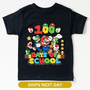 May include: Black t-shirt featuring a graphic of Mario, Luigi, Yoshi, and Toad celebrating 100 days of school. The graphic includes the text "100 Days of School" and has a video game theme.