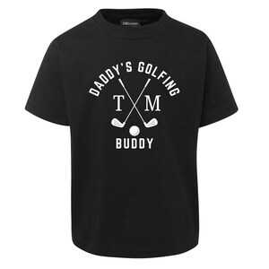 May include: Black t-shirt with white text that reads "Daddy's Golfing TM Buddy". The text is in a circle with two crossed golf clubs and a golf ball.
