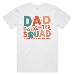 May include: White t-shirt with a colorful graphic design that says "DAD DAUGHTER SQUAD #UNBREAKABLEBOND".