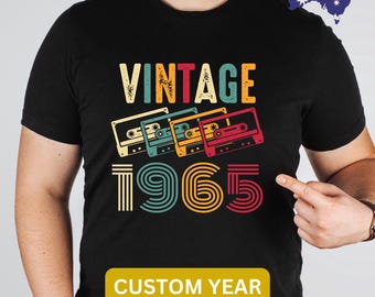 May include: Black t-shirt with a vintage 1965 design featuring a cassette tape graphic. The text "Vintage" is above the year and the text "Custom Year" is below the year.