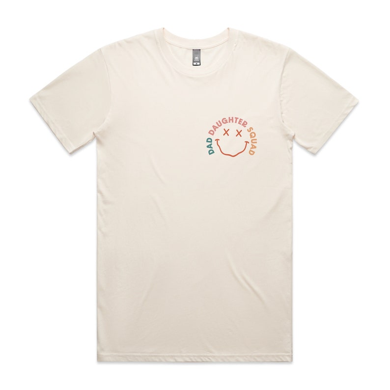 May include: A cream colored t-shirt with a graphic of a smiley face with the text "Dad Daughter Squad" around it.
