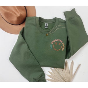 May include: Green sweatshirt with a colorful smiley face graphic that says "Dad Daughter Squad".