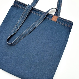 Peut inclure: Un sac fourre-tout en jean bleu avec des anses en cuir marron et une petite étiquette en cuir marron avec le texte "Earthwise" dessus.
