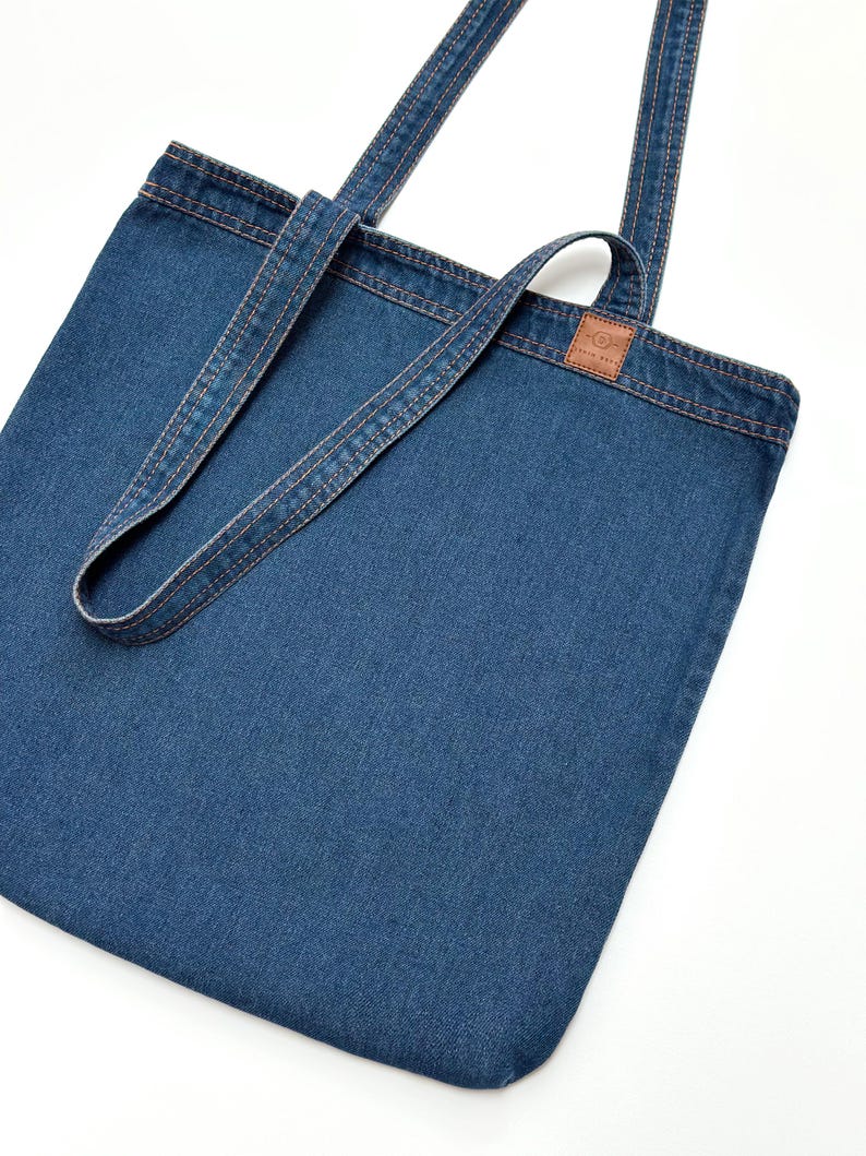 A blue denim tote bag with long handles and a small brown leather label Denim Deko