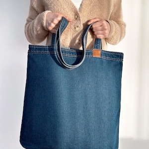 May include: A blue denim tote bag with long handles. The bag is large enough to carry groceries or other items.