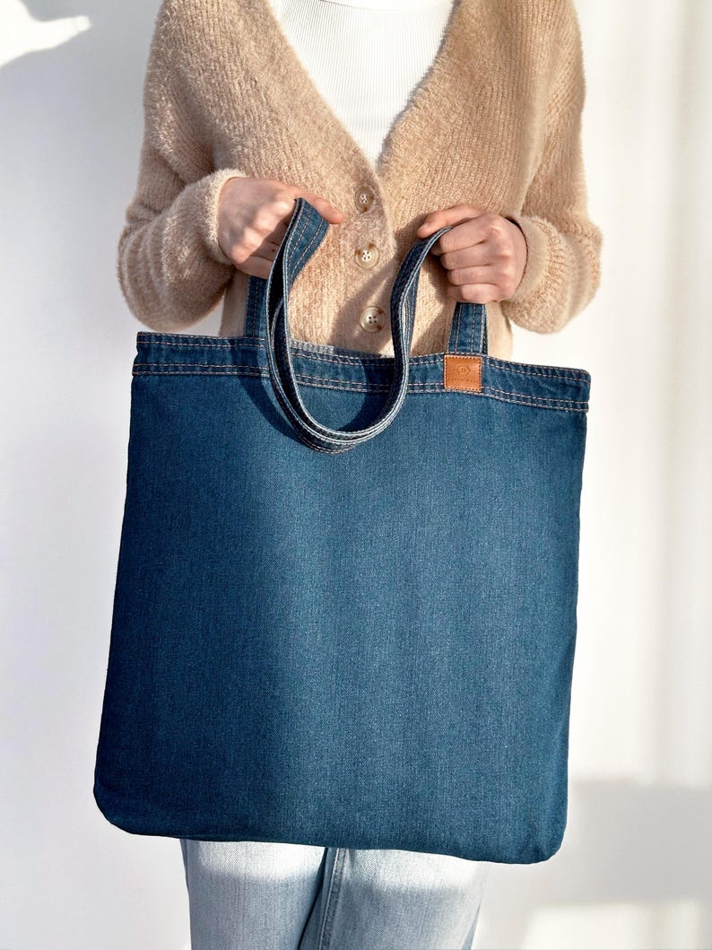 May include: A blue denim tote bag with long handles. The bag is large enough to carry groceries or other items.