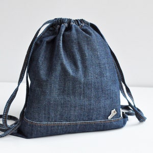 Könnte beinhalten: Eine blaue Jeans-Kordeltasche mit einem kleinen weißen Schuhdesign auf der Vorderseite.