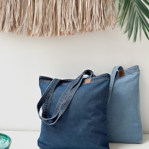 May include: Two denim tote bags, one dark blue and one light blue, with long handles. The bags are sitting on a white surface.