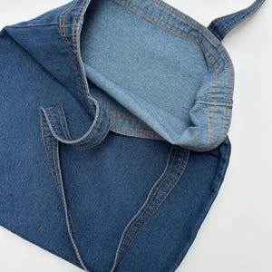 May include: A blue denim tote bag with orange stitching. The bag is folded in half and the inside of the bag is visible.