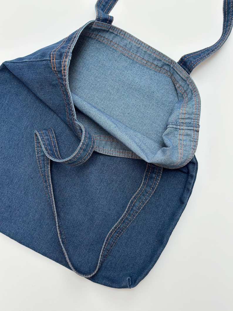 May include: A blue denim tote bag with orange stitching. The bag is folded in half and the inside of the bag is visible.