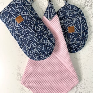 May include: A set of three kitchen accessories in a blue and white geometric pattern. The set includes a potholder, a dish towel, and a hot pad. The dish towel is pink.