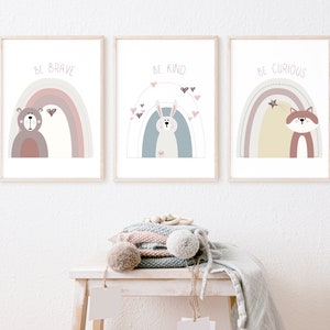 May include: Three framed art prints with pastel rainbows and animal illustrations. The prints read "BE BRAVE" with a bear, "BE KIND" with a bunny, and "BE CURIOUS" with a fox. The artwork is displayed on a white wall.