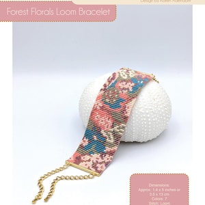 Könnte beinhalten: Ein gewebtes Armband mit floralem Muster in Rosa, Blau und Creme. Das Armband ist ca. 3,5 cm breit und 13 cm lang, mit goldfarbener Kette und Endstücken. Das Design heißt "Forest Florals Loom Bracelet".