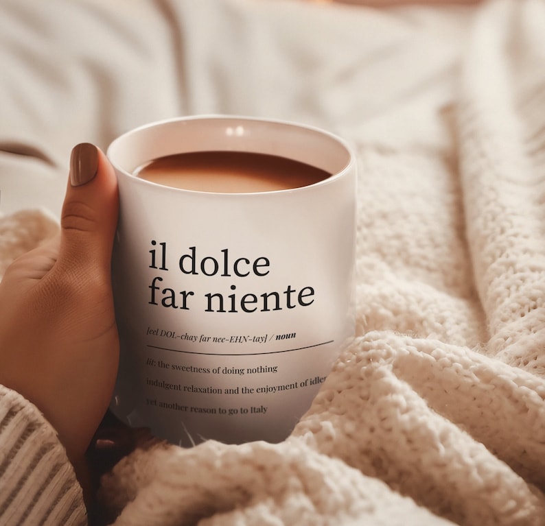 close-up of ceramic mug with italian quote il dolce far niente held in cozy blanket