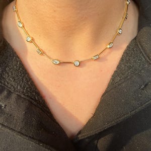 Peut inclure: Un collier doré orné de pierres précieuses claires de forme ronde et baguette. Le collier est conçu pour se porter près du cou. Les pierres sont serties en ligne sur la chaîne dorée. Le collier est un bijou.