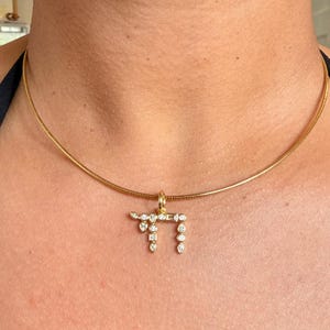 May include: A gold chain necklace featuring a pendant shaped like the Hebrew letter Chai. The pendant is encrusted with multiple small, clear, faceted stones in various shapes, including round, pear, and baguette cuts, set in a gold frame.