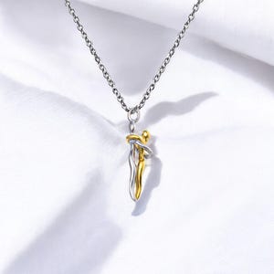 Könnte beinhalten: Silberfarbene Halskette mit einem Anhänger, der zwei sich umarmende Figuren zeigt. Eine Figur ist silberfarben, die andere goldfarben. Der Anhänger hängt an einer zarten Kette vor weißem Hintergrund. Ein Symbol der Liebe und Verbundenheit.