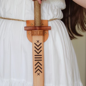 Wooden toy sword with engraved blade and leather sheath, worn on rope belt, medieval role play accessory