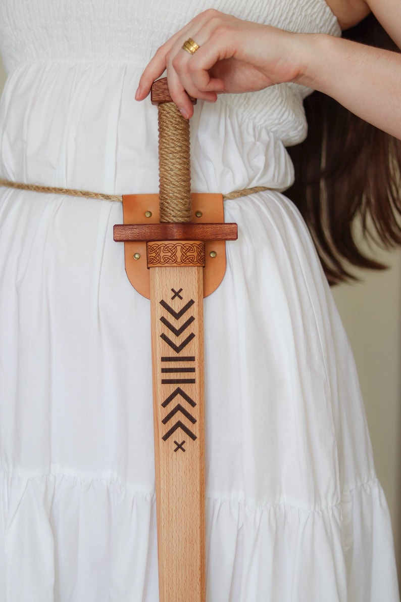 Wooden toy sword with engraved blade and leather sheath, worn on rope belt, medieval role play accessory