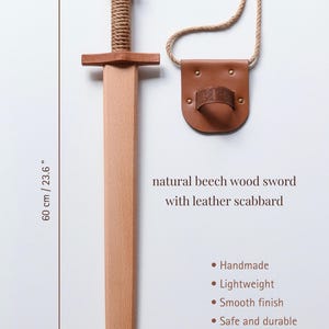 May include: A natural beech wood sword with a rope-wrapped handle and a leather scabbard featuring a rope strap. The sword measures 23.6 inches in length. Text on the image reads: natural beech wood sword with leather scabbard, Handmade, Lightweight, Smooth finish, Safe and durable.