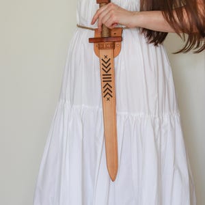 Wooden toy sword with engraved blade and leather sheath, worn on rope belt, medieval role play accessory