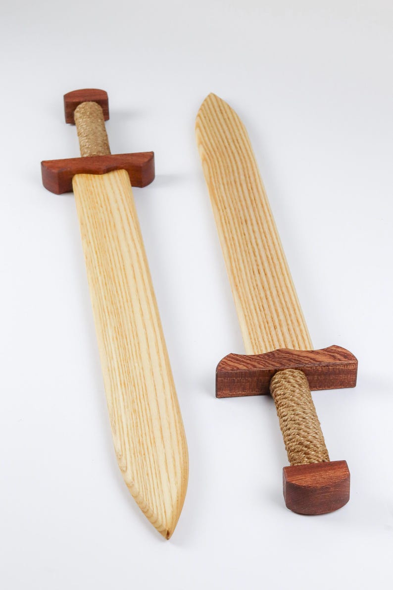 May include: Two wooden swords featuring light-colored blades with visible wood grain, dark reddish-brown wooden crossguards and pommels, and handles wrapped in thick, natural-colored jute rope. The swords are positioned side by side.