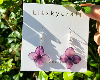 May include: A pair of purple flower earrings with silver hooks. The earrings are made with real pressed flowers and are labeled "Litskycraft Handmade Jewelry".