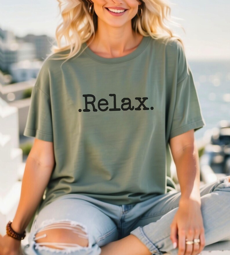 May include: A woman wearing a green t-shirt with the text ".Relax." printed on it. She is wearing ripped jeans and sitting on a wooden surface.