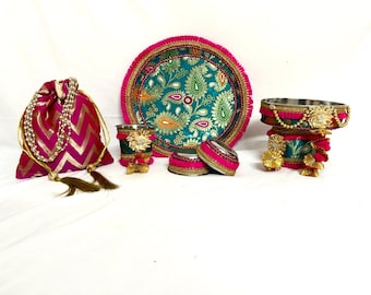 May include: A set of decorative items featuring a pink and gold drawstring bag, a teal and gold patterned plate, and small containers. The items are embellished with pink trim, gold accents, and tassels.