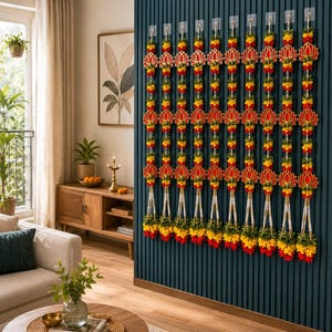 Könnte beinhalten: Dekorative Girlanden hängen an einer dunkelblauen Wand. Jede Girlande hat ein rotes Lotusblumen-Design, gelbe und rote florale Akzente und weiße Perlenstränge. Die Girlanden sind in vertikalen Reihen angeordnet und schaffen eine lebendige und festliche Präsentation.