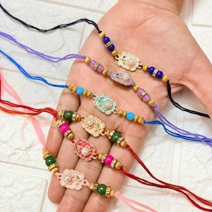 May include: A selection of colourful beaded bracelets with ornate, oval-shaped centrepieces. Each bracelet features a different colour cord, including black, purple, blue, red, and pink, and is adorned with gold-coloured beads and decorative accents. The centrepieces have a floral design.