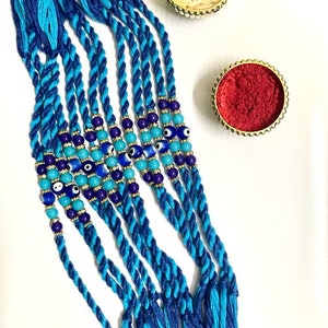 May include: A set of blue and turquoise braided bracelets with evil eye beads and gold accents. The bracelets are arranged on a white surface with small bowls of red powder and white rice.