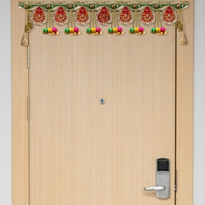 Op de afbeelding: Een traditionele Indiase deurhanger met rode, groene en gouden accenten. De hanger heeft een kralenrand met roze, groene en gele ballen.