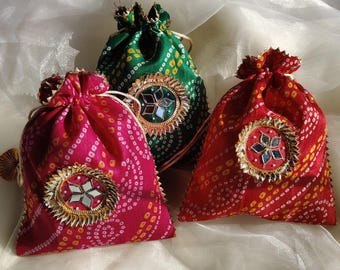 May include: Three small drawstring bags with colorful patterned fabric and decorative embellishments. The bags are red, green, and red with gold accents.