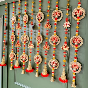 Può includere: Un set di 10 decorazioni per porte con motivi di fiori di loto dorati e rossi. Ogni decorazione presenta un fiore di loto circolare con un centro rosso e petali dorati, circondato da un anello dorato. Le decorazioni sono infilate con perline dorate e rosse e hanno campane dorate in basso.