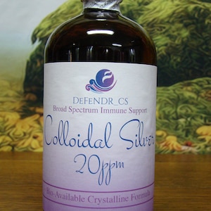 May include: A brown glass bottle with a white and purple label. The label reads "DEFENDR_CS Broad Spectrum Immune Support Colloidal Silver 20ppm". The bottle is sealed with a silver band that reads "SEALED FOR YOUR PROTECTION". The bottle contains 16 fl. oz.