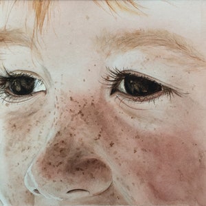Puede incluir: Pintura acuarela de primer plano de la cara de un niño con pecas y ojos marrones. El niño está mirando hacia un lado, y la pintura captura una sensación de inocencia y asombro.